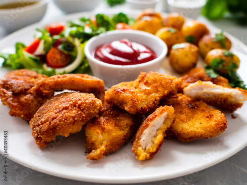 Fried breaded chicken nuggets with fried potatoes and fresh vegetables 