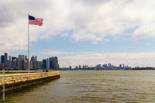 New York City, New York - July 29, 2016: American flag in the foreground with a view of the cityscape of New York in the background in a sunny cloudy day