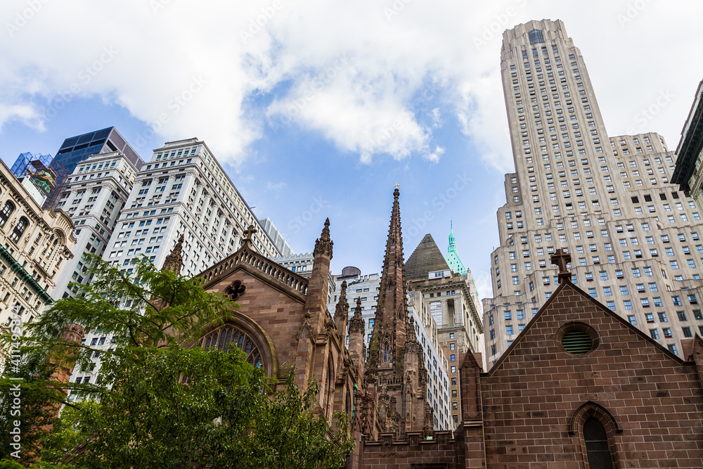 View of the top part of Trinity Church in Financial District in New York with buildings in the background and cloudy blue sky