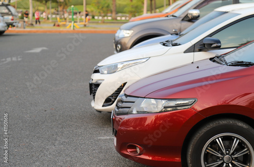 Closeup of front side of red car with other cars parking in outdoor parking area in twilight evening.  © Amphon