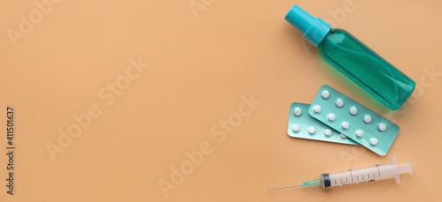 Banner with medical objects on gold sand colour background. Medical syringe, pills and antiseptic flat lay, health and vaccination concept, copy space, top view.