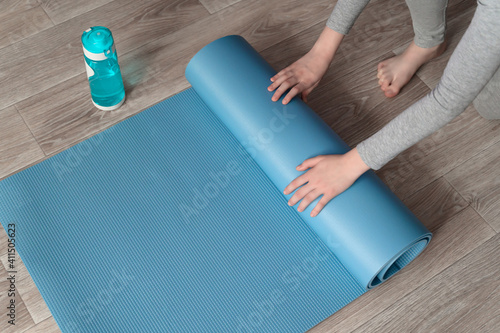 Teenage girl doing fitness exercise, practicing yoga at home. Healthy lifestyle concept. She spreads the yoga mat. Workout at home. Home interior, daytime.