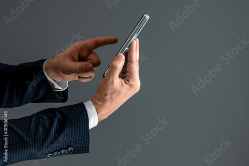Hands of a businessman in a business suit holds a smartphone horizontally side view and presses the screen with his finger. Close-up.