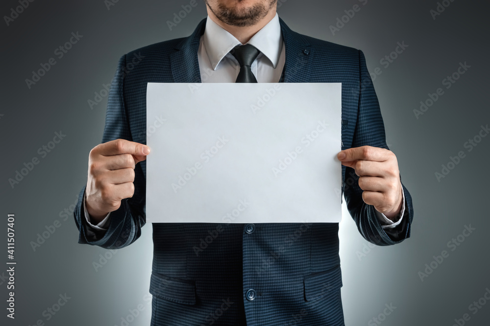 A man in a suit holds a white A4 sheet, mockup, layout. Concept for business lettering, blank. Shot on a gray background. A man in a suit holds a white A4 sheet, mockup, layout. Concept for business lettering, blank. Shot on a gray background.