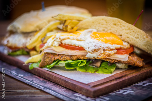 Milanesa argentinian steak sandwich with salad tomatoes cheese egg, chips and beer