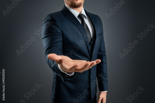 Foto Male hand in a suit shows a palm up gesture on a gray background