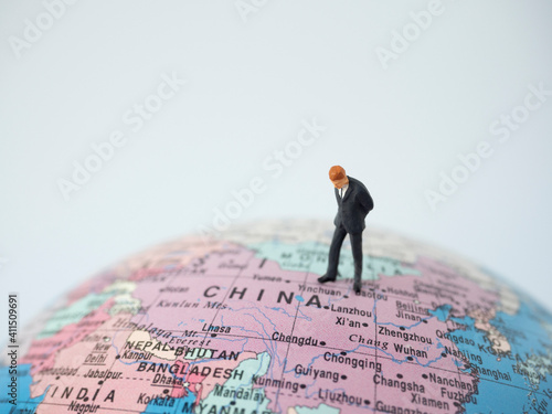 Miniature figure businessman standing on china map and look at map globe as business economic or world business competition concept.