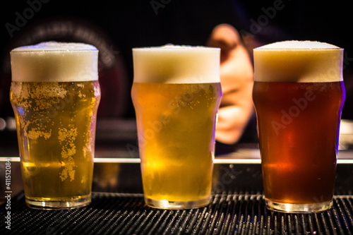 Billede på lærred Three pints of tap beer lager, blonde and amber on in a bar with bartender