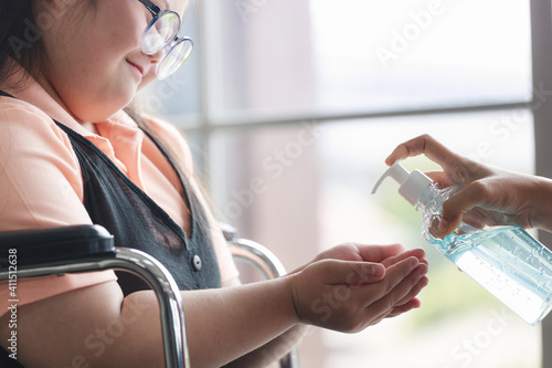 A mother teaches an Asian autistic girl who sits in a wheelchair to wash his hands with alcohol gel in the coronavirus covid-19 epidemic. Stay at home. New normal.
