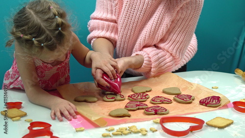 Girl and mom decorate cookies in the form of a heart with pink sweet icing. Making cookies for Valentine's Day