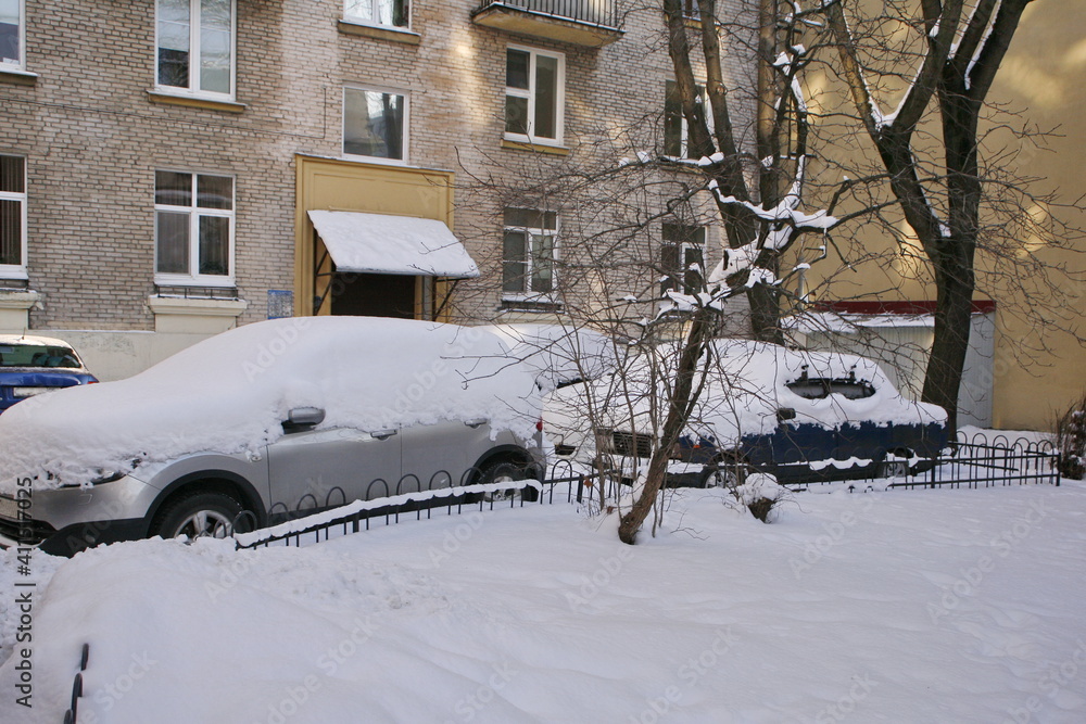 Uncleaned courtyards with heavy snowdrifts after snowfall in the city, cars under the snow.