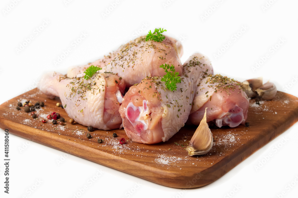 Raw chicken drumstick on a wooden cutting board, spices for cooking chicken drumsticks, parsley, pepper and salt, suneli hops. Isolate. Side view Raw chicken drumstick on a wooden cutting board, spices for cooking chicken drumsticks, parsley, pepper and salt, suneli hops. Isolate. Side view