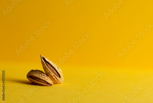 Fototapeta Naklejka Na Ścianę i Meble -  Two unpeeled almonds on a yellow background. Side view and copy space. Horizontal orientation