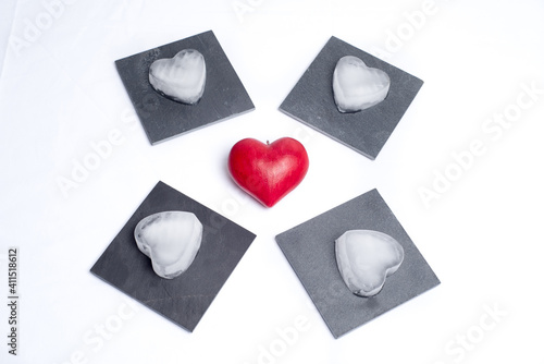 Top view on a red love heart and 4 slate plates with ice hearts on them, on a white background