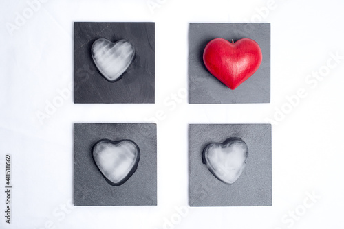 One red love heart and 3 hearts made of ice, placed on 4 slate plates, on a white background. Graphic and geometric, concept of love