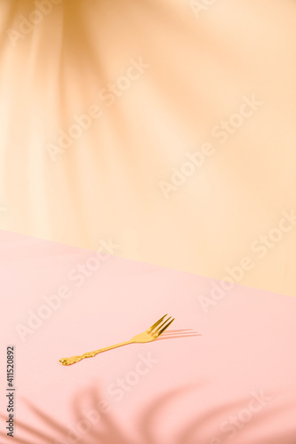Minimal creative concept of single gold fork against nice pastel pink background with palm leaves shadow in the corners. Celebration idea © Sasa Lalic