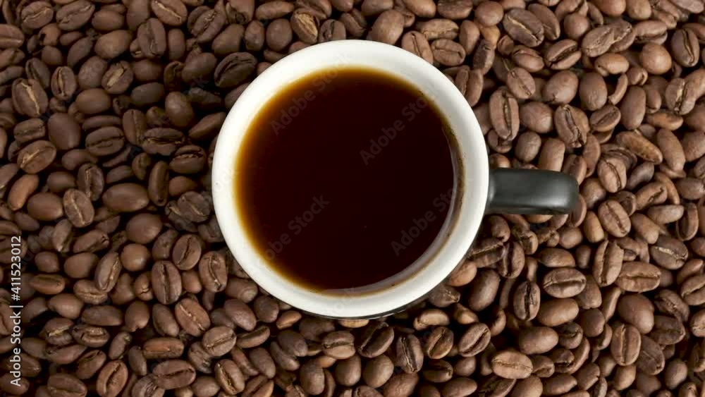 Cup of coffee with fresh roasted coffee beans background, close-up circular rotation, high angle view Cup of coffee with fresh roasted coffee beans background, close-up circular rotation, high angle view