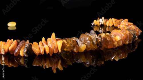 A dazzling necklace made of different types of natural amber close-up on a black background with a reflection.