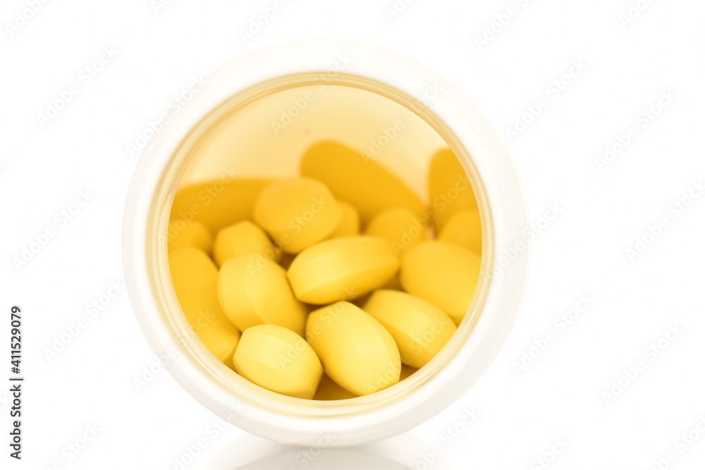Several oval yellow pills with a white plastic box, close-up, isolated on white. Several oval yellow pills with a white plastic box, close-up, isolated on white.