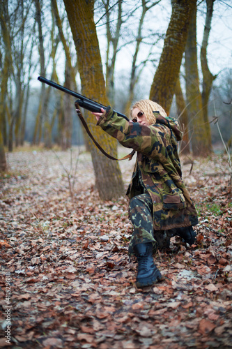 caucasian woman in camouflage suit and sunglasses aim a shotgun in the autumn forest