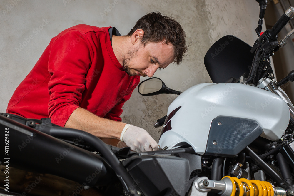 Young man repairing or preparing a motorbike for a new season after winter time, basic motorcycle maintenance Young man repairing or preparing a motorbike for a new season after winter time, basic motorcycle maintenance