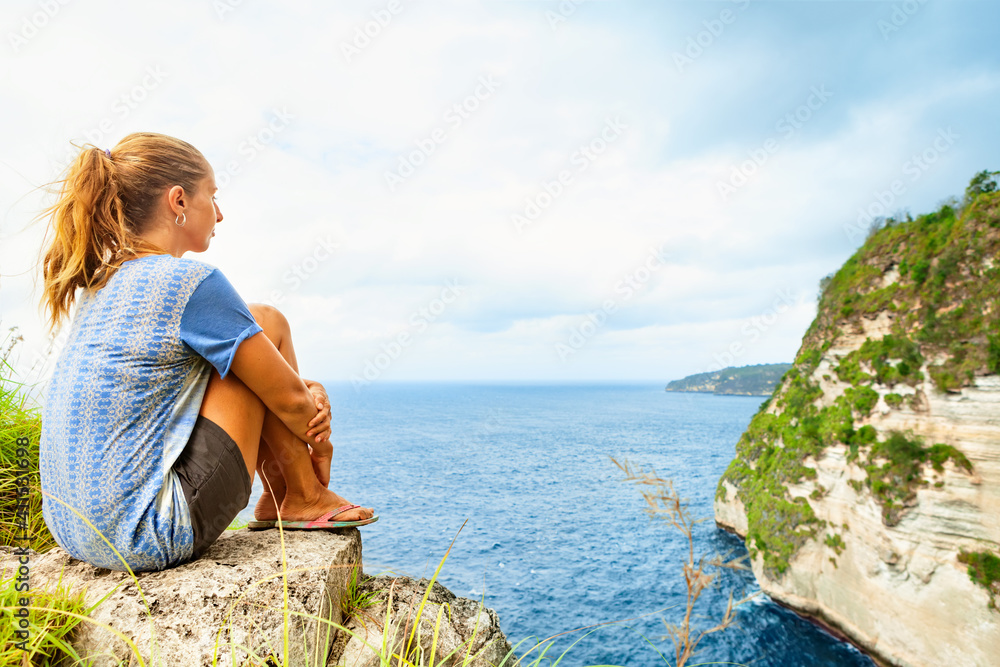 Happy girl have fun on summer beach holiday. Young woman relax at rock cliff above sea. Looking at beautiful view of coast. Healthy family lifestyle, summer travel on tropical island.