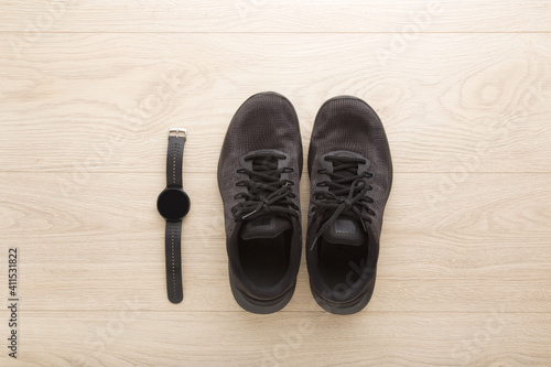 Black male sport shoes and smartwatch for walking, running or fitness on wooden floor background. Closeup. Top down view.
