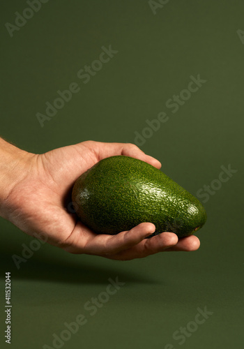 Studio shot of ripe avocado on male hand isolated over green background. Vegan food, healthy lifestyle concept