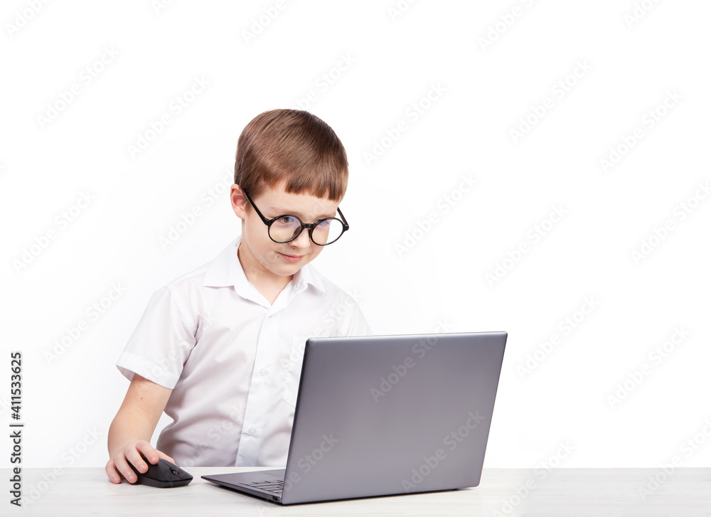 a boy with glasses, an elementary school student, sits at a table with a laptop on a white background a boy with glasses, an elementary school student, sits at a table with a laptop on a white background