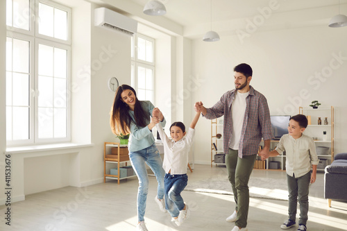 Smiling young parents and cheerful kids daughter and son having fun together at home on weekend with light spacious room interior at backgroundFamily spending happy time at home with children concept