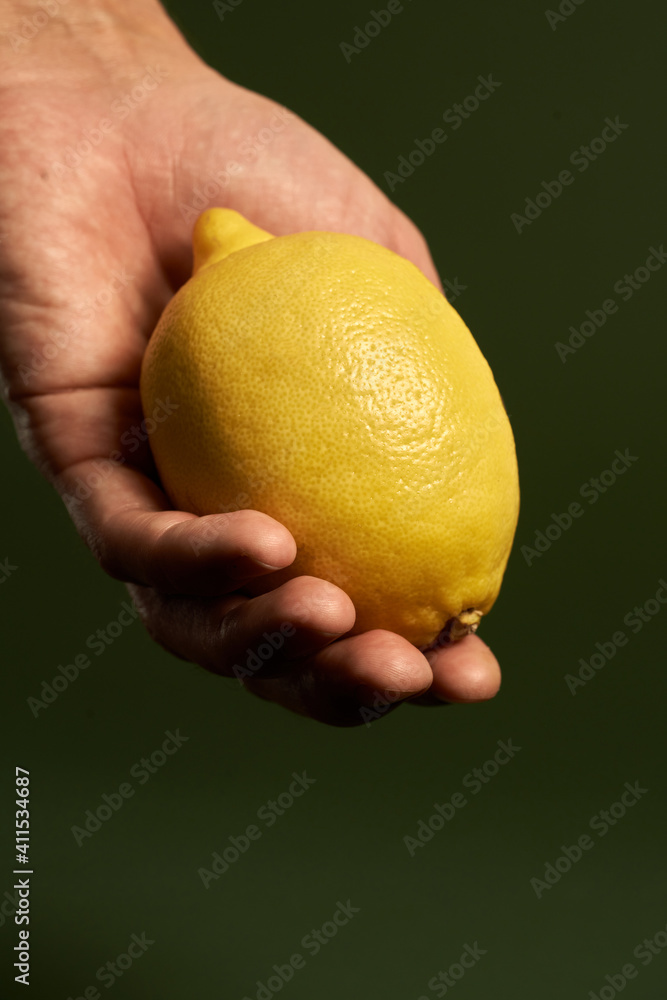 Studio shot of ripe yellow lemon on male hand isolated over green background. Healthy eating and diet concept Studio shot of ripe yellow lemon on male hand isolated over green background. Healthy eating and diet concept