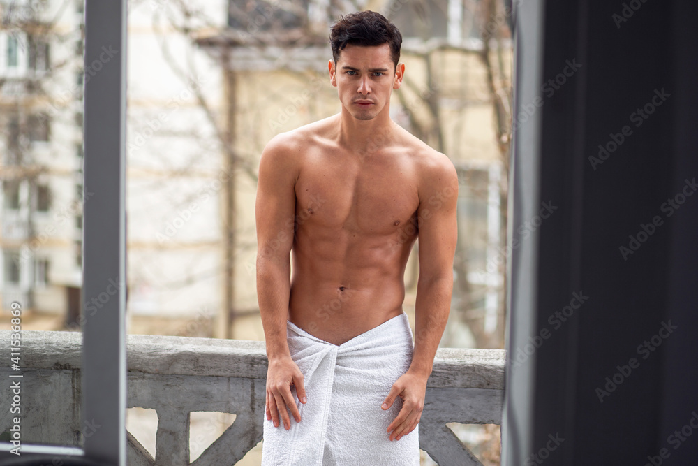 Fototapeta premium Strong sexy handsome young man poses on balcony with naked torso outside.