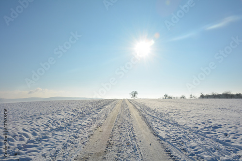 Snow-covered road in the country, a lot of snow in the fields with sky and sun