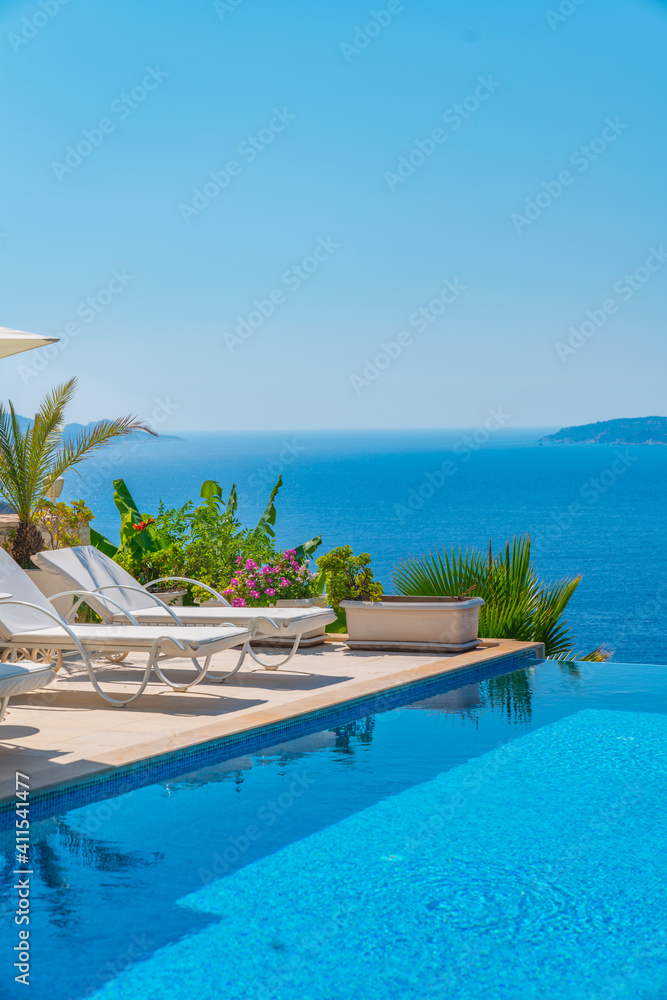 Summer vacation at poolside. Veranda decorated with deck chairs and umbrella with an ocean view. Swimming pool overlooking the sea