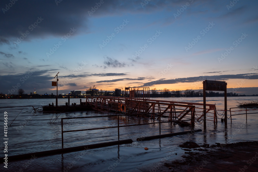 Outdoor scenery view of flooded area along riverside of Rhine river in Düsseldorf, Germany during evening time with beautiful sunset and twilight sky.