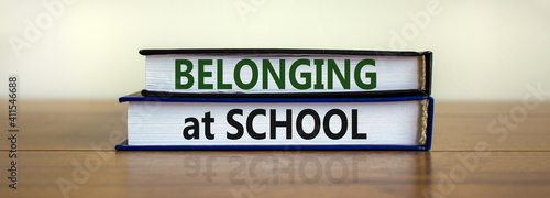 Belonging at school symbol. Books with words 'Belonging at school' on beautiful wooden table, white background. Business, belonging at school concept. Copy space.