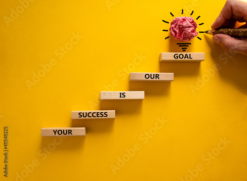 Business concept growth success process. Wood blocks stacking as step stair on yellow background, copy space. Businessman hand. Words 'your success is our goal'. Conceptual image of motivation.