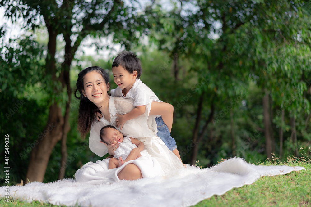 Asian young beautiful mother holding her newborn is sleeping and feel with love and touching gently then sitting on green grass in the park Asian young beautiful mother holding her newborn is sleeping and feel with love and touching gently then sitting on green grass in the park