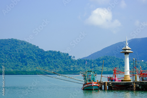 wooden boat near pier and small white tower in island. big mountain behind blue sea