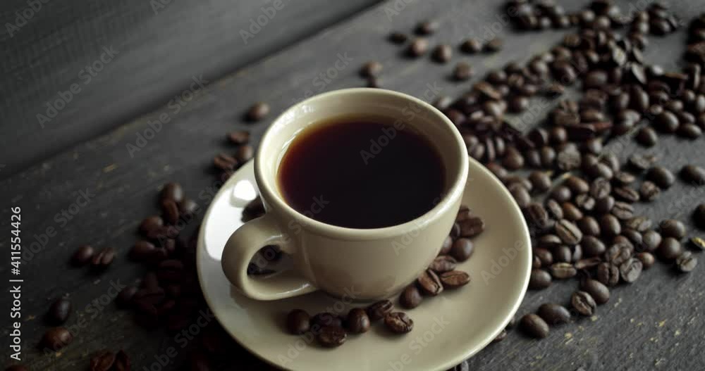 Cup of coffee with roasted coffee beans scattered on a wooden table. Mug of fresh black coffee. Fresh arabica roasted coffee beans. Great start of perfect morning. Espresso, americano, doppio. Cup of coffee with roasted coffee beans scattered on a wooden table. Mug of fresh black coffee. Fresh arabica roasted coffee beans. Great start of perfect morning. Espresso, americano, doppio.