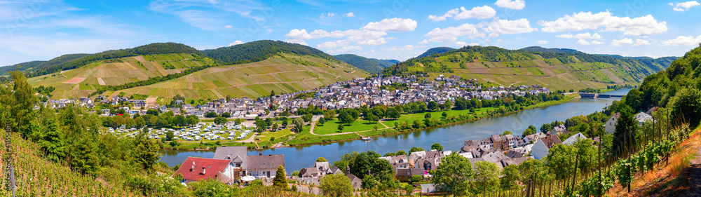 Enkirch, Rhineland-Palatinate, Germany. Panoramic view of the river Moselle with the village Enkirch and the surrounding vineyards of the Moselle valley on a sunny afternoon.