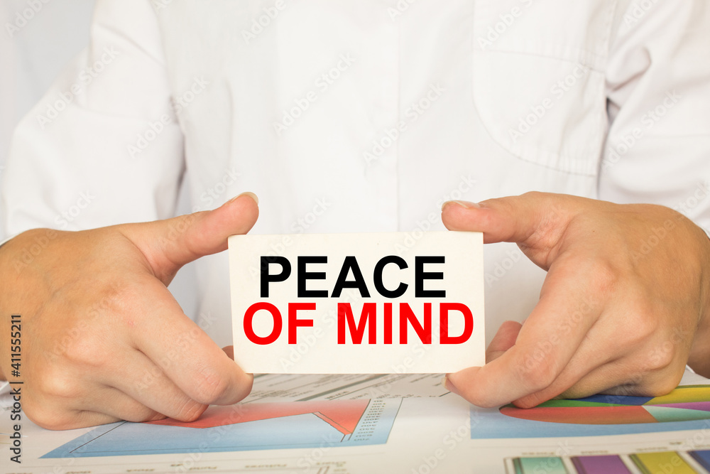 a man in the office holds a card with text PEACE OF MIND . business concept a man in the office holds a card with text PEACE OF MIND . business concept