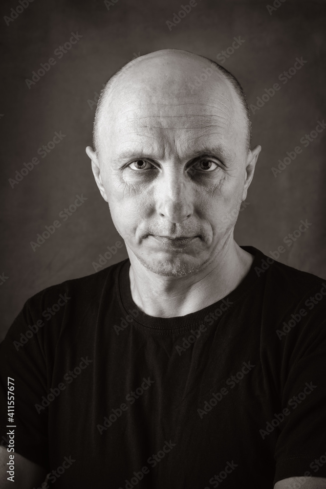 A serious middle-aged man with an unshaven face and a bald head, looking directly into the camera. Black and white portrait toned in sepia. Photo taken in studio A serious middle-aged man with an unshaven face and a bald head, looking directly into the camera. Black and white portrait toned in sepia. Photo taken in studio