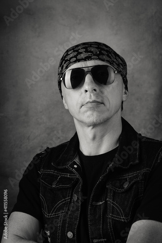 Unshaven, middle-aged man in a T-shirt, denim vest, bandana and sunglasses. Black and white portrait. Photo taken in studio