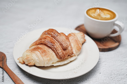 cup of coffee and Fresh baked croissant on white kitchen table. Top view with copyspace for your text.