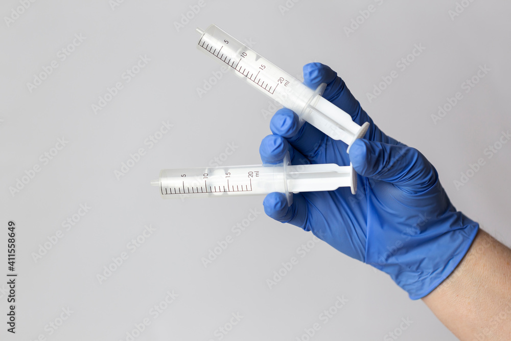 Obraz premium A human hand in a blue protective glove holds twoo syringes between his fingers. White background.