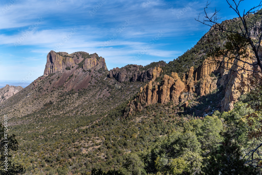 A flat top craggy mountain a part of a larger ridge with colorful rocky cliffs and trees on the slops, Casa Grande Peak, Big Bend National Park, Texas