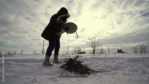 The witchdoctor conjures the spirits of fire with a stone on a tambourine near the fire in the snow photo