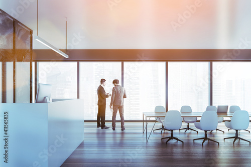 Two colleagues discussing clients business case before the meeting in modern panoramic office in downtown. reception area and fulllengthwindows. Lens flare