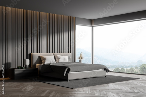 Corner of master bedroom with grey wooden walls, panoramic window with countryside view, comfortable king size bed standing on gray carpet and parquet floor. photo